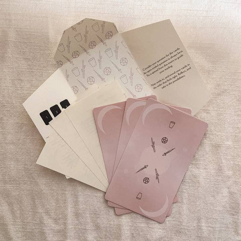 Set of pink tarot cards with a patterned card and envelope on a textured surface