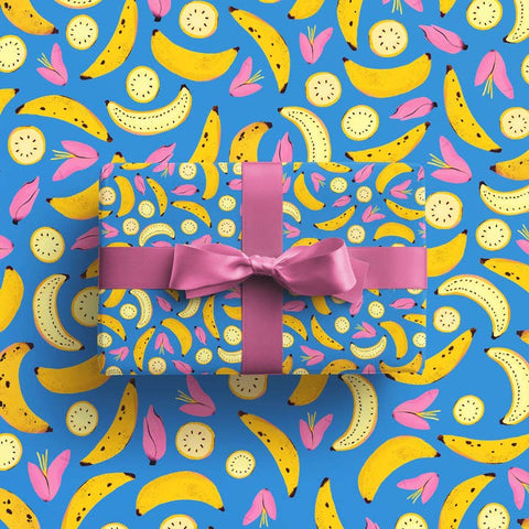 Present with a pink ribbon on a blue background with banana and kiwi pattern