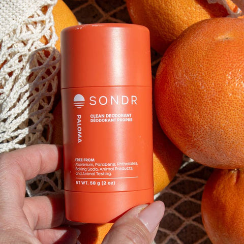 Orange SONDR deodorant stick held in front of oranges