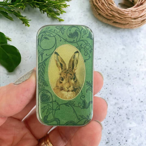 Green decorative tin with rabbit illustration held by a hand on a textured surface.