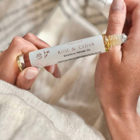 Hand holding a 'Rose & Cedar' botanical perfume oil roller bottle.