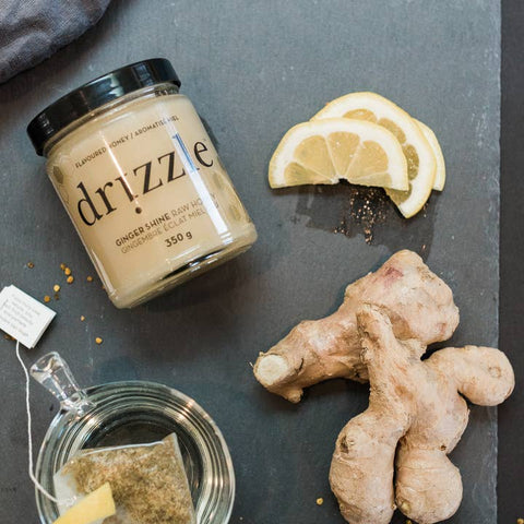 Jar of driizzie ginger lemon honey on a dark surface with ginger root and lemon slices.