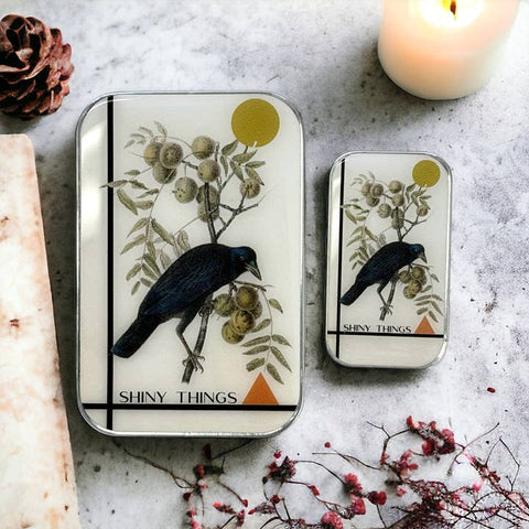 Two small rectangular containers with bird illustrations on a textured surface with flowers and a candle.
