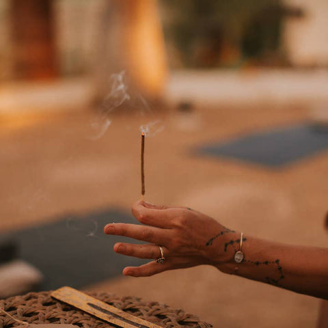 Hand holding a smoking incense stick with a blurred outdoor background
