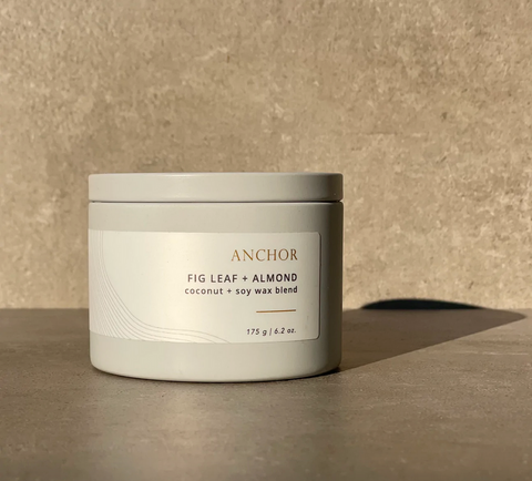 Candle jar labeled 'Anchor' with 'Fig Leaf + Almond' scent on a beige background