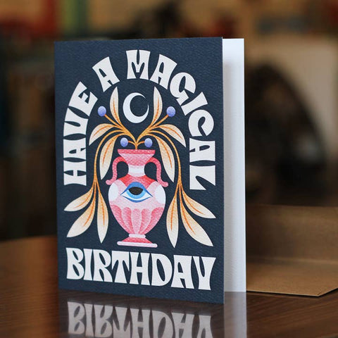 Greeting card with 'Have a Magical Birthday' text and decorative urn design on a dark blue background.