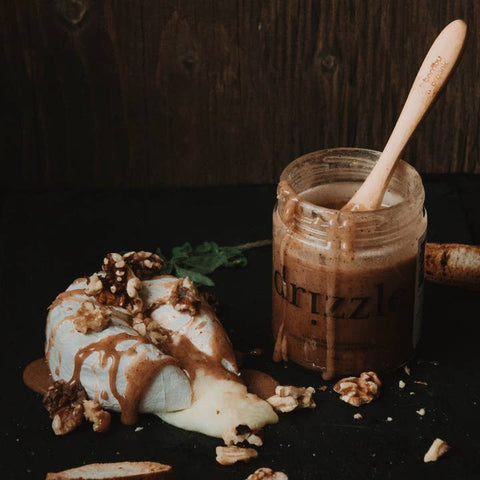 Jar of chocolate spread with a spoon, next to a dessert with cinnamon drizzle on a dark background