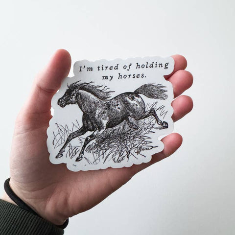 Hand holding a sticker with a horse illustration and text on a white background