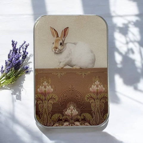 Decorative tin with a rabbit illustration on a white surface with lavender flowers.