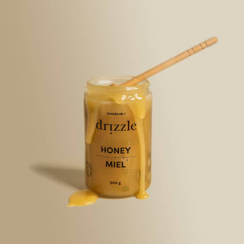 Jar of drizzle honey with a wooden spoon on a beige background