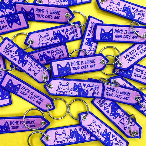 Purple and blue keychains with cat illustrations and text on a yellow background