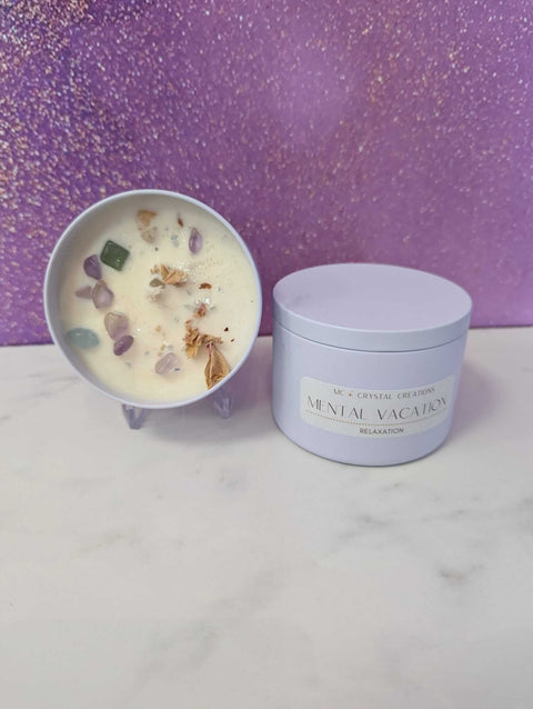 Candle with decorative stones in a bowl next to a container labeled 'Mental Vacation' on a white surface with purple glittery background.