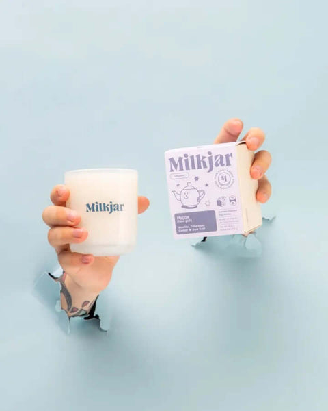 Hand holding a Milkjar mug and packaging against a light blue background