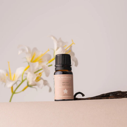 A bottle of Scentuals essential oil with flowers in the background on a beige surface.