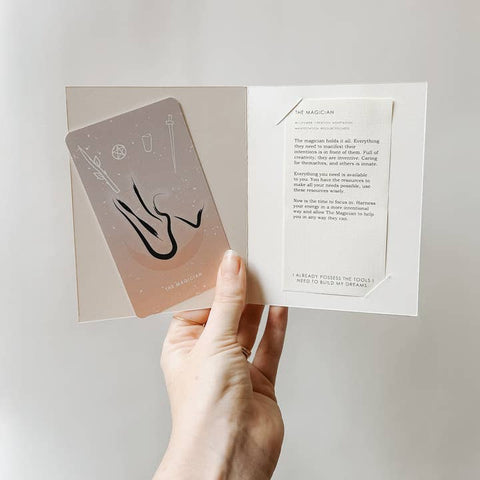 Hand holding a tarot card with text on a light background