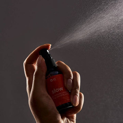 Hand holding a red spray bottle labeled 'slow' against a dark background