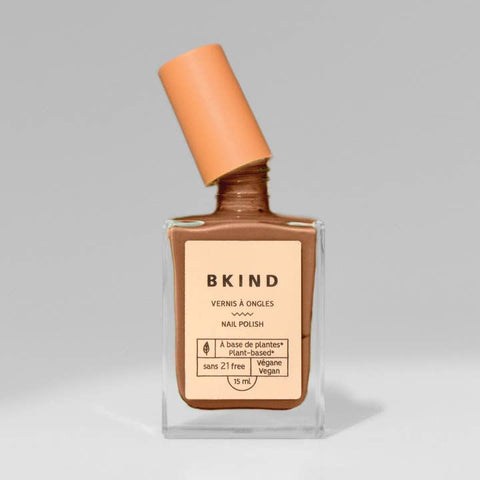 Bottle of BKIND nail polish with a brown shade on a gray background
