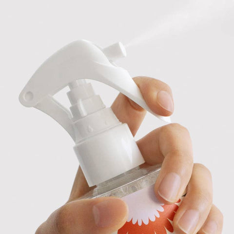 Hand holding a white spray bottle with a Dandylion label against a light gray background