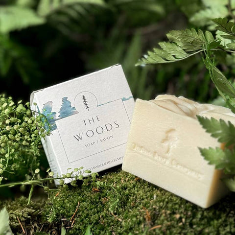 Bar of soap and packaging labeled 'The Woods' on a green leafy background