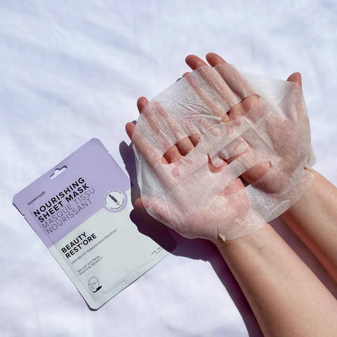 Person applying a sheet mask with a package labeled 'Nourishing Sheet Mask' on a light background