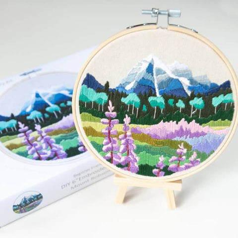 Embroidery hoop with mountain and flower design on a white background