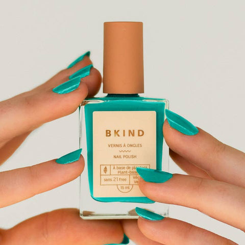 BKind nail polish bottle held by hands with teal nail polish on a light background