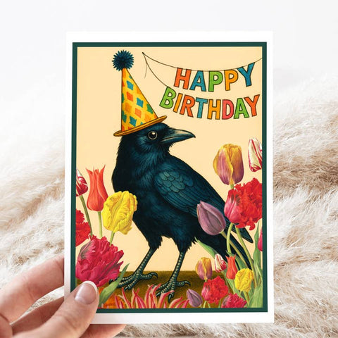 Birthday card with a black bird wearing a party hat and colorful tulips on a textured surface