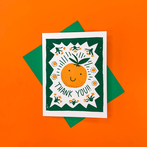 Card with a smiley orange and 'Thank You!' text on a green background, placed on an orange surface.