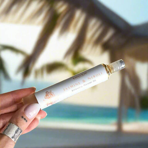Hand holding a bottle of 'Jasmine & Neroli' botanical perfume oil with a blurred tropical background.
