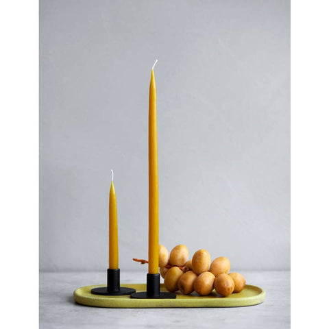 Two yellow taper candles in black holders on a matching oval tray, styled with small decorative eggs against a light gray background.