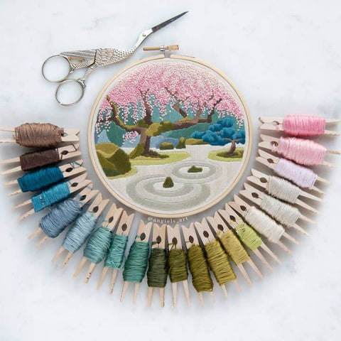 Embroidery hoop with cherry blossom tree design surrounded by colorful threads and scissors on a white background