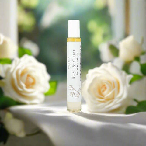 Roll-on bottle of 'Rose & Cedar' perfume with white roses in the background