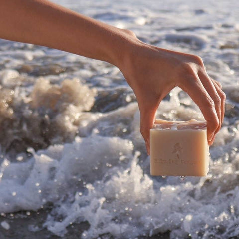 Hand holding a bar of soap over water with a blurred background