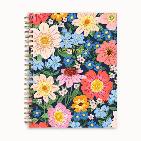 A spiral-bound notebook with a colorful floral pattern on a navy blue background. The cover features large flowers in pink, peach, orange, blue, and yellow, with green leaves.