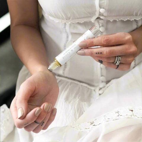 Person holding a pen with a white and gold design, wearing a white dress.