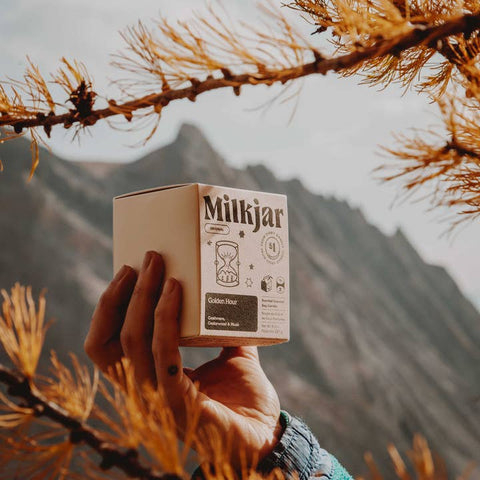 Hand holding a 'Milkjar' product box with a mountainous background