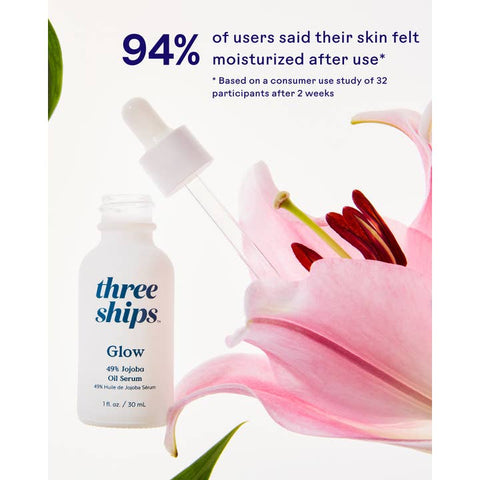Three Ships Glow serum bottle with dropper and pink flower on a white background