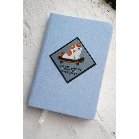 Light blue notebook with a cat patch on a textured white surface