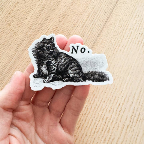 Sticker of a cat with 'No.' text held in a hand on a wooden surface