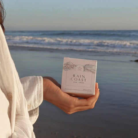 Person holding a 'Rain Coast' soap bar on a beach