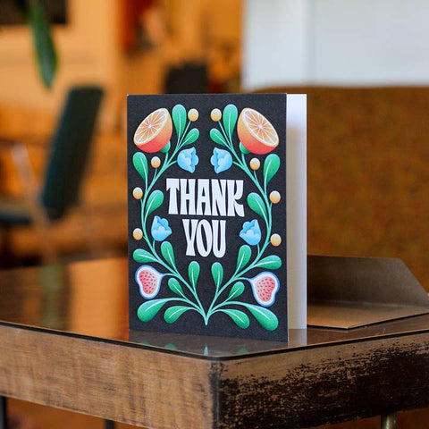 Greeting card with floral design and 'Thank You' text on a wooden surface.
