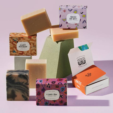 Collection of handmade soaps with decorative boxes on a light purple background