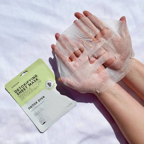 Detoxifying sheet mask being applied to a hand with a visible packaging label on a white background