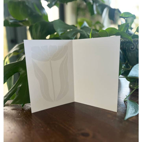 White card with leaf pattern on a wooden surface with green leaves in the background