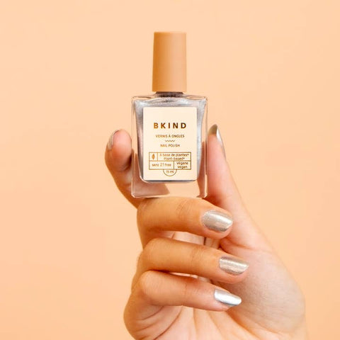 Hand holding a bottle of BKIND nail polish against a peach background