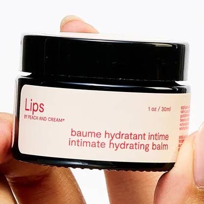 Jar of 'Lips' intimate hydrating balm held by a hand on a white background