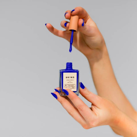 Hand holding a small bottle of skincare product with a dropper, against a gray background.