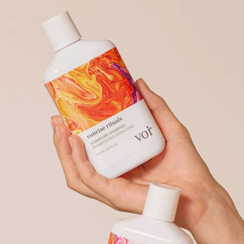 Hand holding a Voir shampoo bottle with colorful label against a beige background