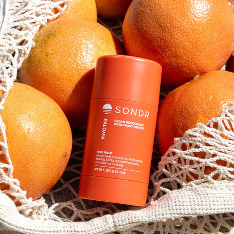 SONDR deodorant stick surrounded by oranges on a textured surface
