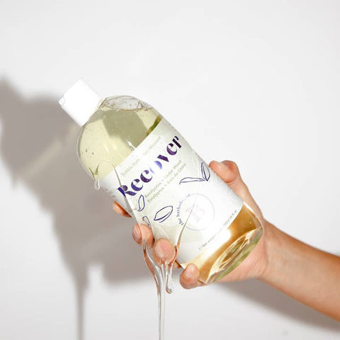 Hand holding a bottle of Recover with a white background